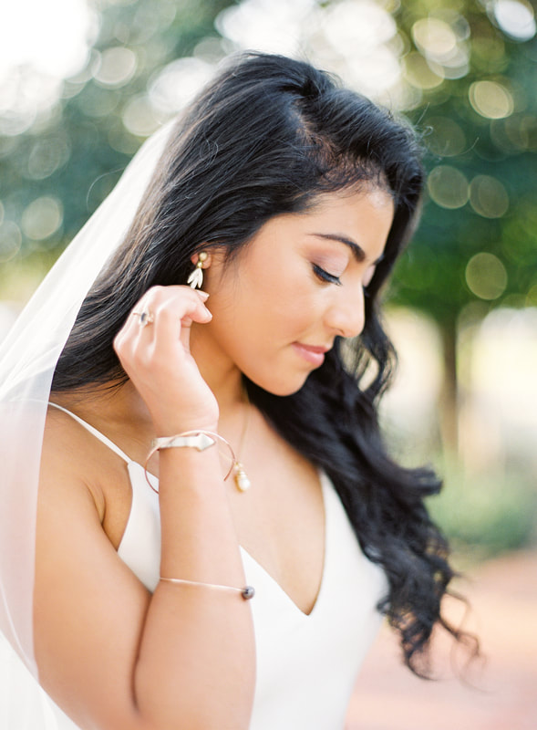 Beautiful Persian bride on her wedding in Texas day looking down at the ground will gently touching her ear.